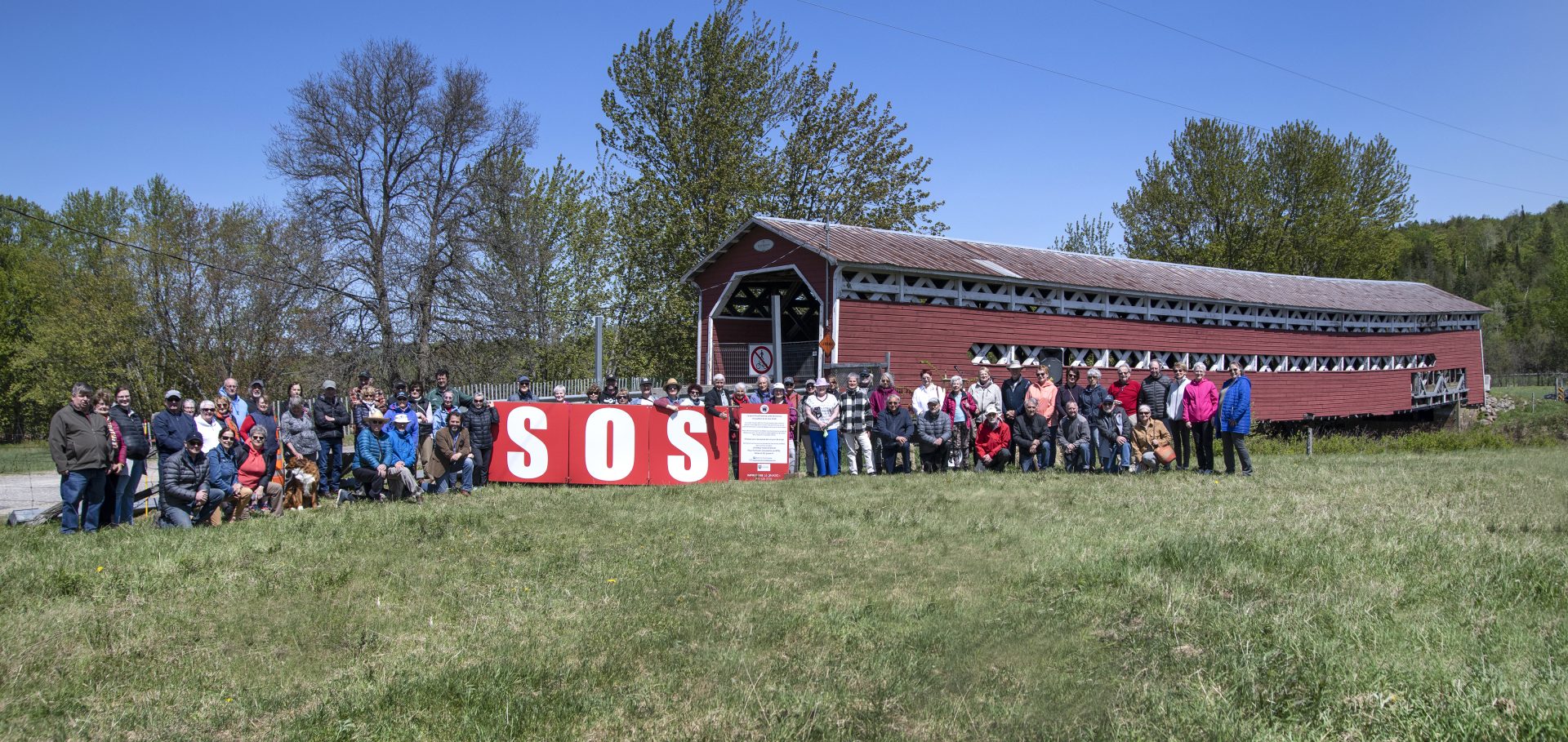 Pancarte SOS rouge et blanche avec pont couvert derrière